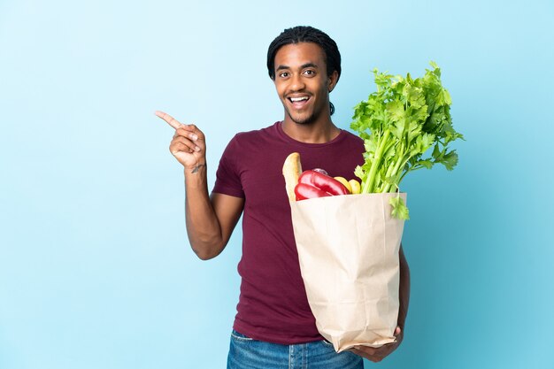 African American man holding un sac d'épicerie isolé sur un mur bleu dans l'intention de réaliser la solution tout en levant un doigt