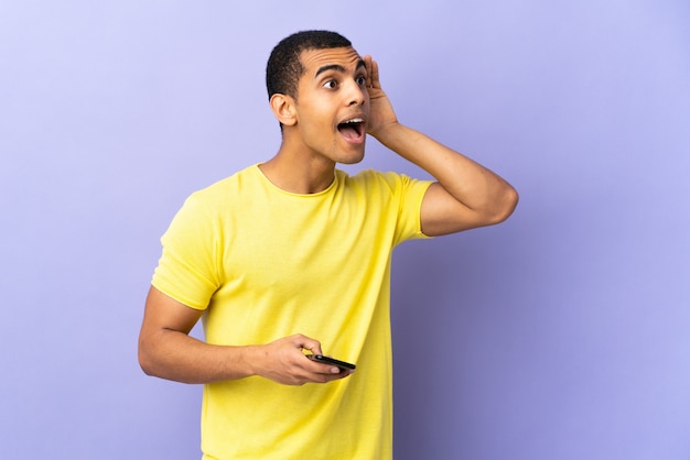 African American man sur violet isolé à l'aide de téléphone mobile écoute quelque chose