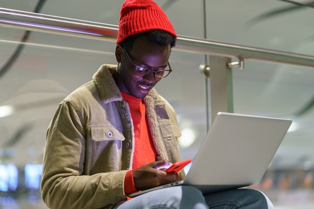 African American traveller homme millénaire au repos et assis sur le sol à l'aéroport à l'aide de téléphone portable