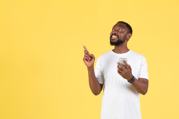 African Man Holding Phone pointant les doigts de côté sur fond jaune