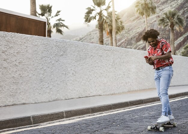 African man riding longboard sur la route avec des palmiers en arrière-plan - Focus sur le visage