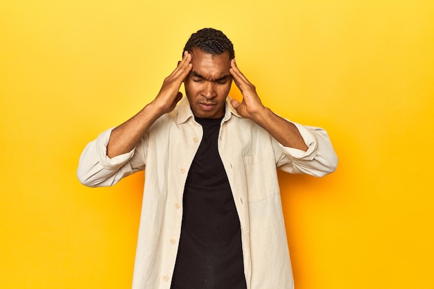 Un Afro-Américain en chemise jaune touche les tempes et a mal à la tête.
