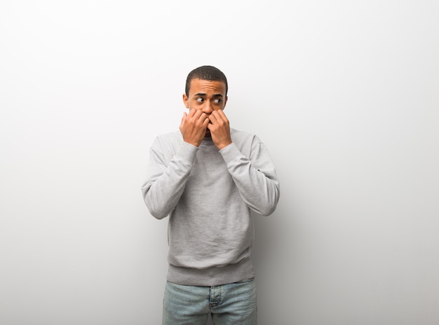 Afro-américain sur fond de mur blanc est un peu nerveux et peur de mettre les mains à la bouche