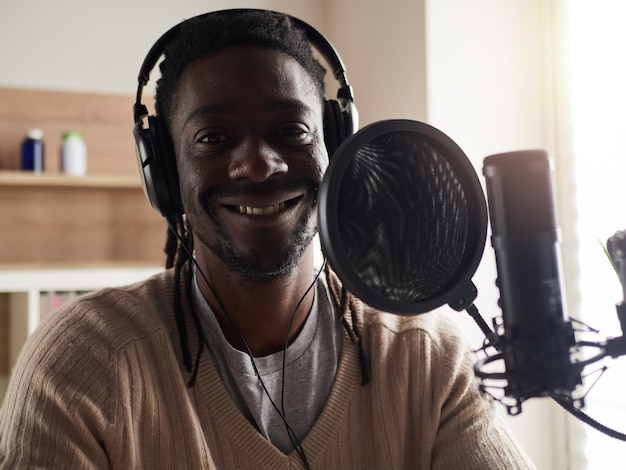 Afro-américain heureux jeune homme enregistrant un blog audio dans un casque microphone diffusant à la maison