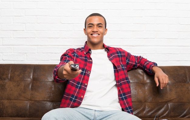 Afro-américain avec ordinateur portable dans le salon avec une télécommande de télévision