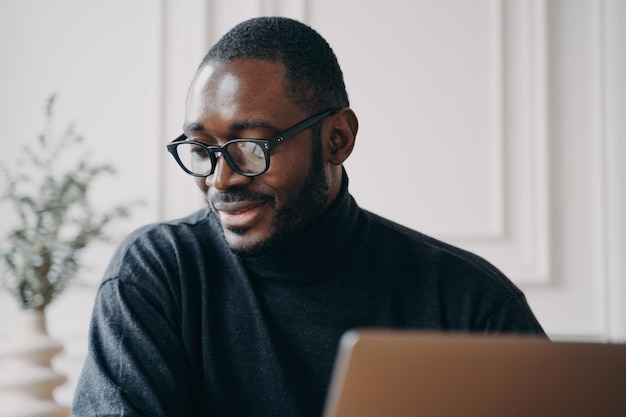 Un afro-américain pensif est assis au bureau à la maison et regarde un cours vidéo en ligne ou un webinaire sur ordinateur