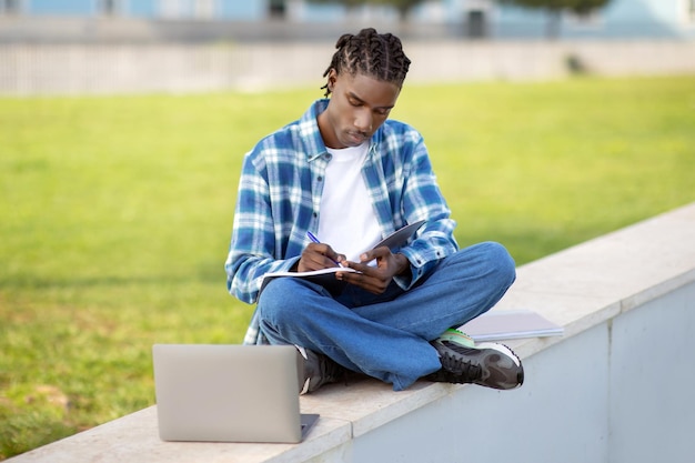 Un Afro-Américain prend des notes dans un carnet de travail et surfe sur le web en plein air.