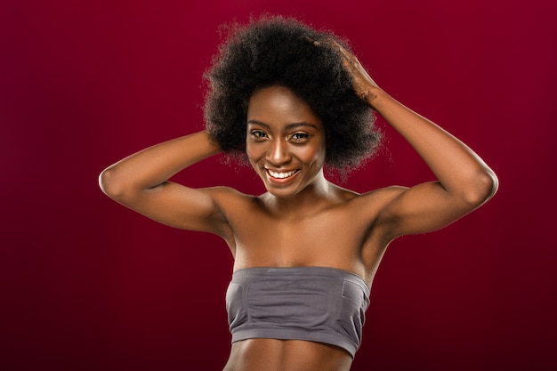 Afro américain. Ravie de femme aux cheveux noirs debout contre le mur rouge tout en posant pour une photo