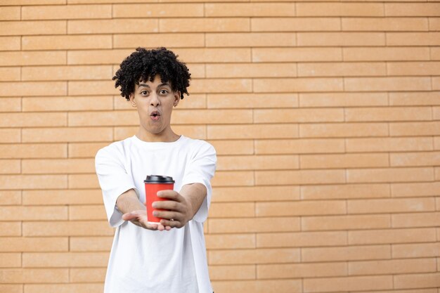 Un afro-américain surpris tenant une tasse de café rouge devant lui portant un t-shirt blanc