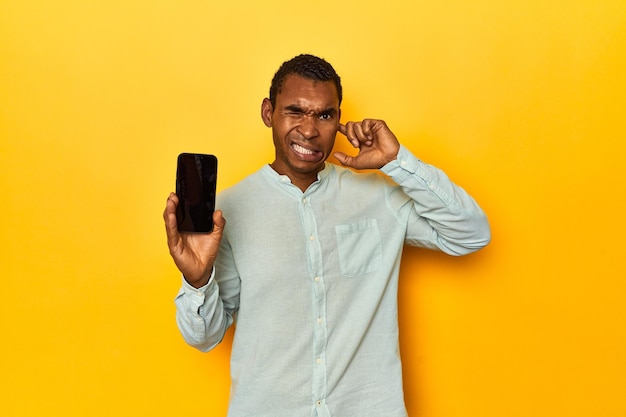 Un Afro-Américain avec un téléphone portable, un studio jaune couvrant les oreilles avec ses mains.