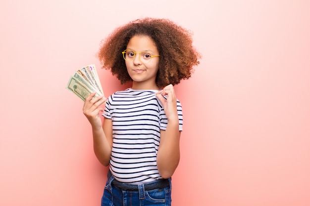 Afro-américaine petite fille contre un mur plat avec des billets en dollars