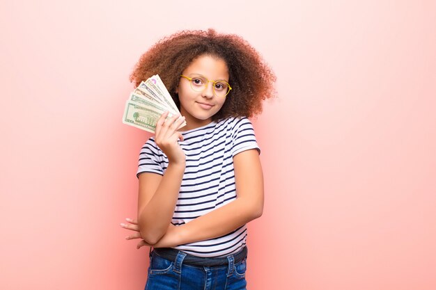 Afro-américaine petite fille contre un mur plat avec des billets en dollars