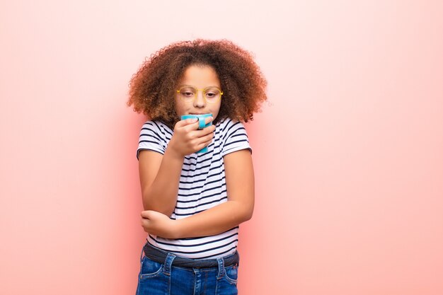 Afro-américaine petite fille contre un mur plat avec une tasse de café