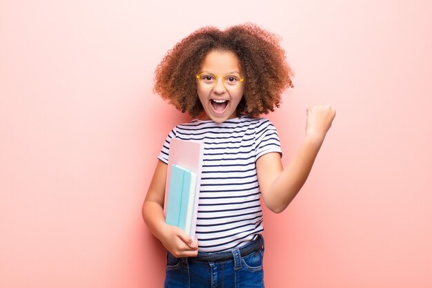 Afro-américaine petite fille contre un mur plat tenant un livre