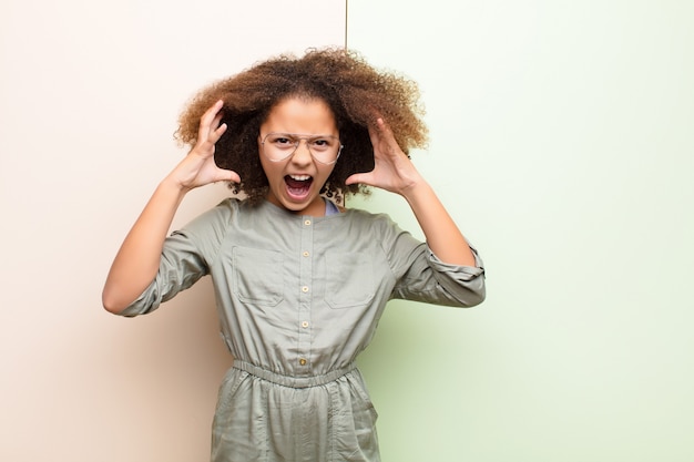 Photo afro-américaine petite fille crier avec les mains en l'air, se sentir furieux, frustré, stressé et bouleversé par-dessus le mur