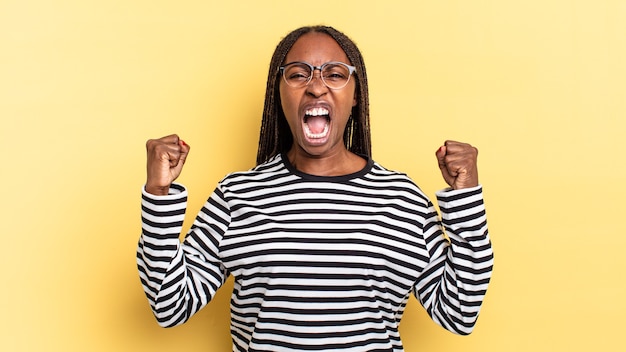 Afro black jolie femme criant agressivement avec une expression de colère ou avec les poings serrés célébrant le succès