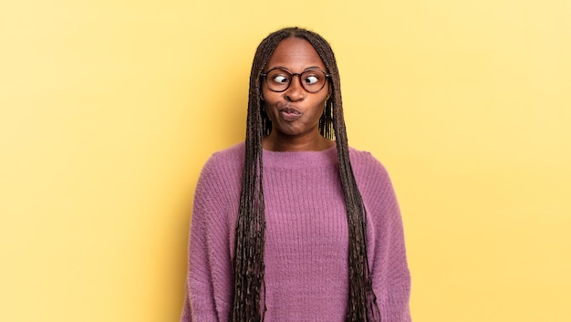 Afro black jolie femme à la recherche maladroite et drôle avec une expression stupide aux yeux croisés, plaisantant et s'amusant