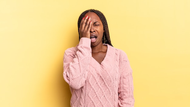 Afro black jolie femme somnolent, s'ennuie et bâille, avec un mal de tête et une main couvrant la moitié du visage