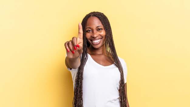 Afro black jolie femme souriante fièrement et avec confiance faisant triomphalement la pose numéro un, se sentant comme un leader