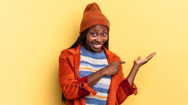 Afro black jolie femme souriante joyeusement et pointant pour copier l'espace sur la paume sur le côté, montrant ou faisant la publicité d'un objet