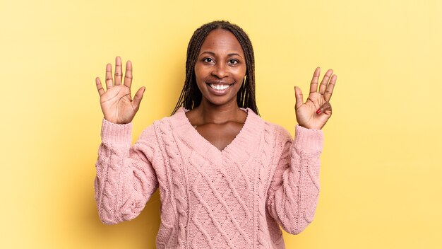 Afro black jolie femme souriante et semblant amicale, montrant le numéro neuf ou neuvième avec la main en avant, compte à rebours