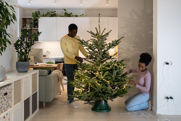 Afro couple rire décorer l'arbre de noël joyeux homme et femme se préparent à célébrer noël ensemble