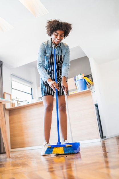 Afro femme balayant le sol avec un balai à la maison.