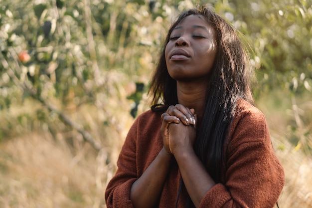 Photo afro girl aux yeux fermés, priant à l'extérieur