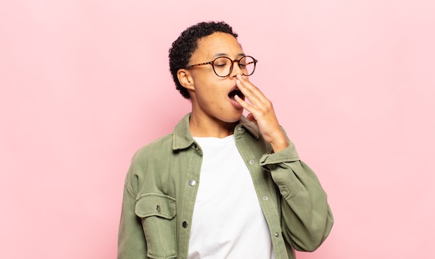 Afro jeune femme noire bâillant paresseusement tôt le matin, se réveillant et à la somnolence, fatiguée et ennuyée