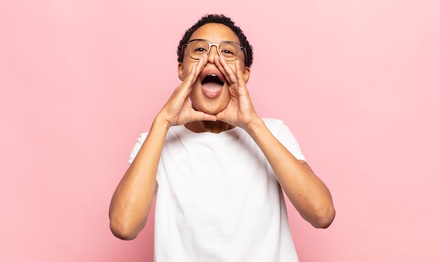 Afro jeune femme noire se sentant heureuse, excitée et positive, donnant un grand cri avec les mains à côté de la bouche, appelant