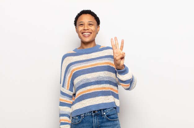 Afro jeune femme noire souriante et à la recherche amicale, montrant le numéro trois ou troisième avec la main en avant, compte à rebours