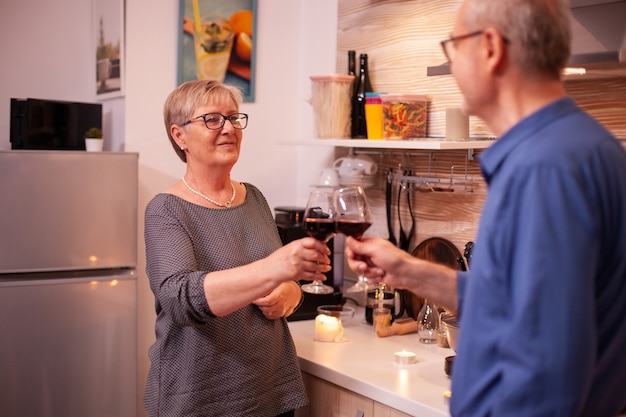 D'âge Mûr Se Regardant Tenant Des Verres De Vin Rouge Le Soir. Couple âgé Amoureux De Parler D'avoir Une Conversation Agréable Pendant Un Repas Sain.