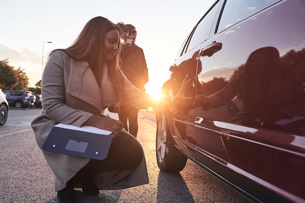 L'agent d'assurance examine la voiture pendant que le conducteur parle au téléphone mobile Processus de réclamation d'accident Femme afro-américaine vérifiant les dommages à la voiture après un accident Concept de transport