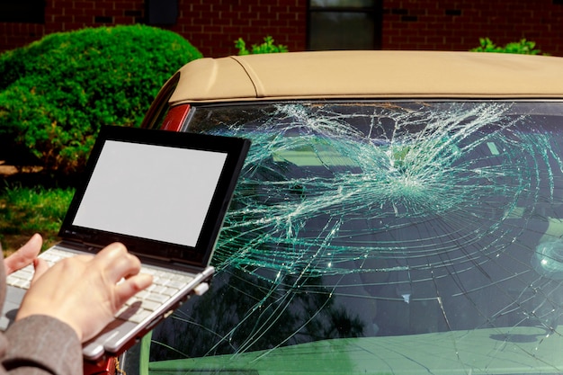 Agent d&#39;assurance remplissant un formulaire de réclamation sur un ordinateur portable après un accident de voiture, un crash de pare-brise