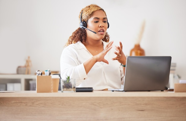 Agent de centre d'appels féminin parlant au casque tout en faisant un appel vidéo ou zoom et travaillant dans un bureau