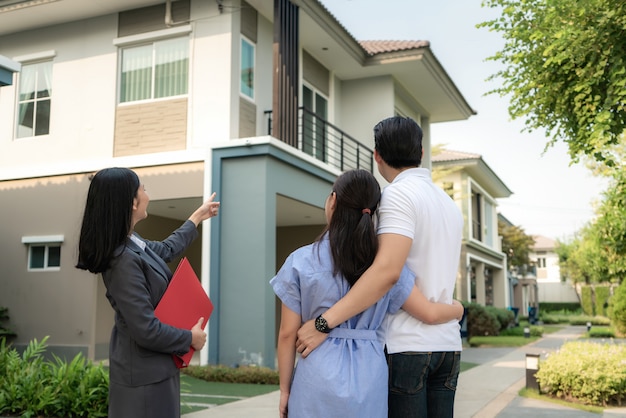 Agent de courtier immobilier femme asiatique montrant un détail du projet de maison dans son dossier au jeune couple amoureux asiatique à la recherche et l'intérêt de l'acheter.
