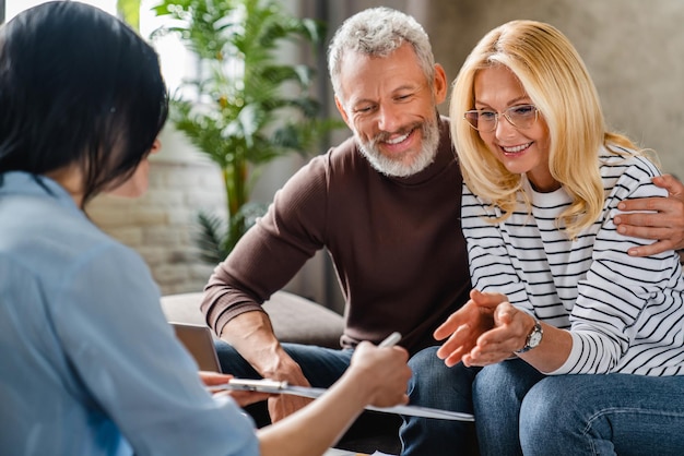 Agent immobilier ou conseiller financier montrant les termes du contrat à un couple heureux sur le bloc-notes