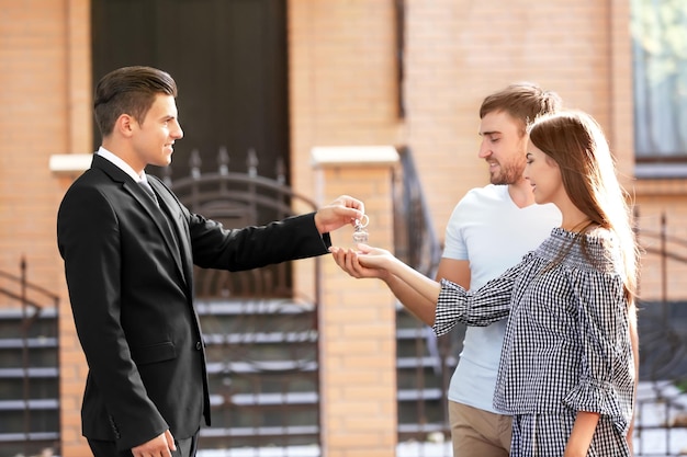 Agent immobilier donnant la clé à un jeune couple près de la maison