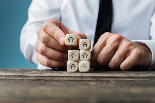 Agent immobilier empilant des dés en bois avec forme de maison sur eux dans une image conceptuelle.