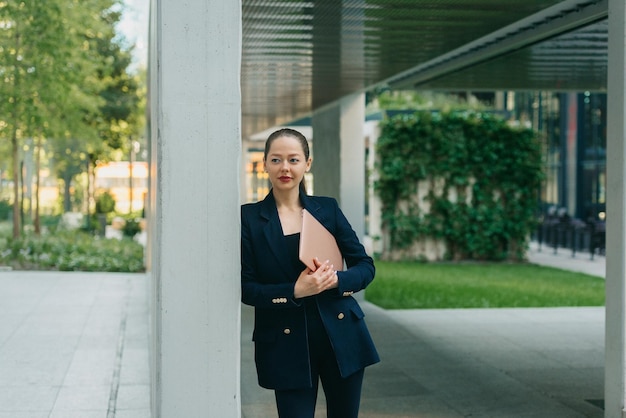 L'agent immobilier féminin dans un blazer tient un ordinateur tout en s'appuyant contre le mur