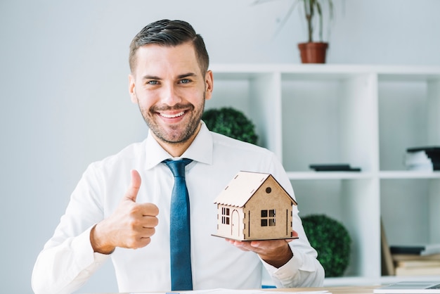 Photo agent immobilier avec la maison de jouet gesticulant thumb-up