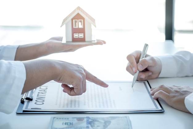 L'agent immobilier pointe la main et explique le contrat commercial, le loyer, l'achat, l'hypothèque, un prêt ou une assurance habitation à l'acheteur.