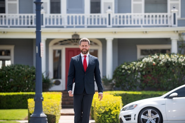 Agent immobilier prêt à vendre un homme d'affaires à domicile debout à l'extérieur d'une maison moderne