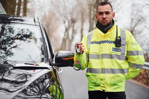 Agent de police masculin en uniforme vert avec des menottes près de l'automobile.