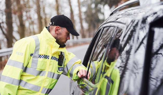 Agent de police masculin en uniforme vert vérifiant le véhicule sur la route.