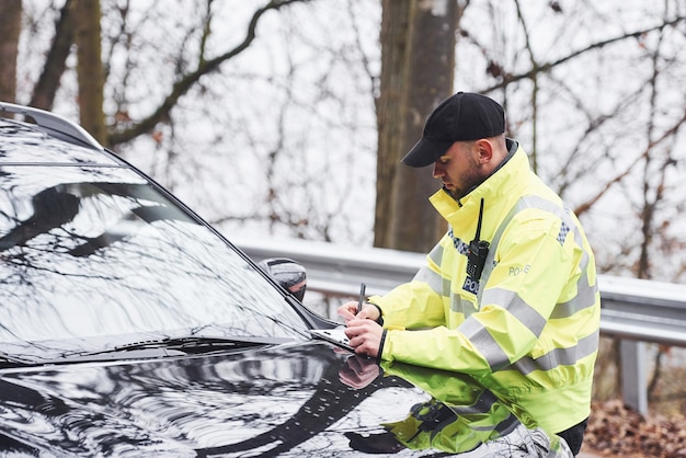 Agent de police masculin en uniforme vert vérifiant le véhicule sur la route.