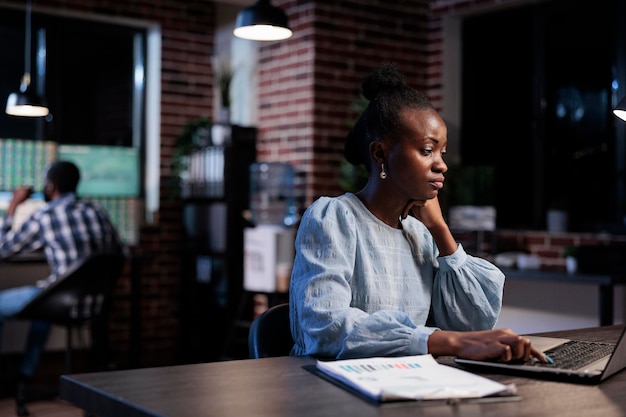 Agent professionnel de la société commerciale assis dans un espace de travail de bureau tout en utilisant un ordinateur portable pour analyser les graphiques du marché. Conseiller financier au travail, examinant la documentation d'investissement tout en essayant de prédire la tendance.