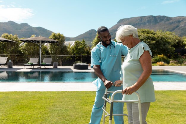 Photo agent de santé afro-américain aidant une femme âgée de race blanche à marcher avec un déambulateur
