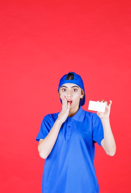 Agent de service féminin en uniforme bleu présentant sa carte de visite et a l'air effrayé.