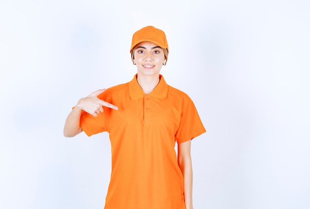 Agent de service féminin en uniforme orange pointant sur elle-même